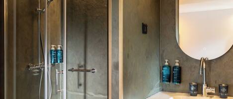 A bathroom with a glass-enclosed shower, a white sink, and toiletries on the countertop.