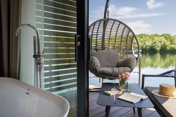A modern bathroom with a bathtub, a hanging chair, and a table with a book and flowers. - L'Escale Royale Torcy - Marne la Vallée (Torcy)