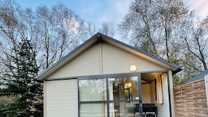 Una casa a un piano con un'ampia porta finestra, un piccolo portico e un interno visibile con tavolo e sedie da pranzo.
