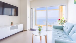 A modern living room with a sofa, a TV mounted on the wall, a small table with a plant, and a balcony with a view. - Intempo by Holuxe - 272 - 27th floor (Benidorm)