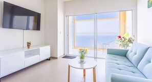 A modern living room with a sofa, a TV mounted on the wall, a small table with a plant, and a balcony with a view. - Intempo by Holuxe - 272 - 27th floor (Benidorm)