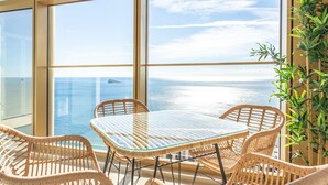 Un balcon avec des fauteuils en osier et une table en verre donnant sur la mer.