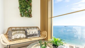 Un balcon avec un canapé en osier, une table en verre ornée de plantes et une vue sur la mer.