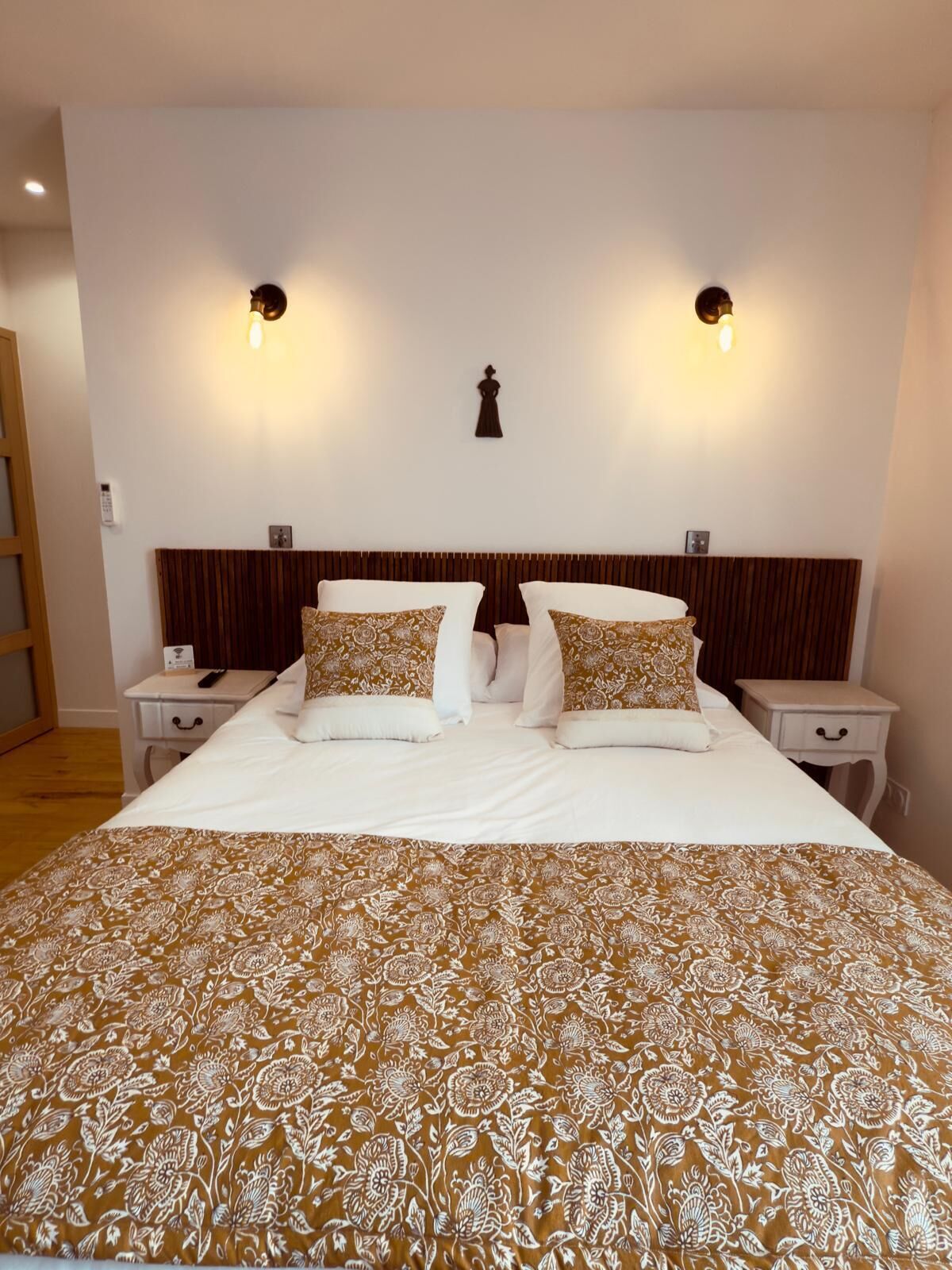 Une chambre d’hôtel avec un grand lit, deux tables de chevet, une tête de lit en bois et deux appliques murales.