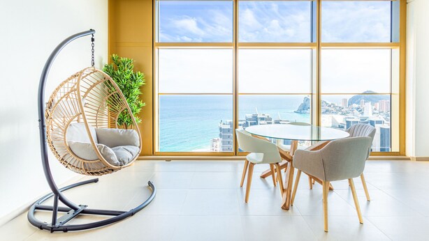 Een moderne woonkamer met een groot raam, een hangstoel, een ronde glazen tafel en twee stoelen.