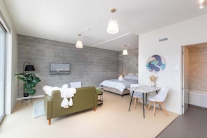 A modern bedroom with a bed, a sofa, a desk with chairs, a TV, and a plant. - Petone 2BR | Near Jackson St + Beach | Kitchen (Lower Hutt)