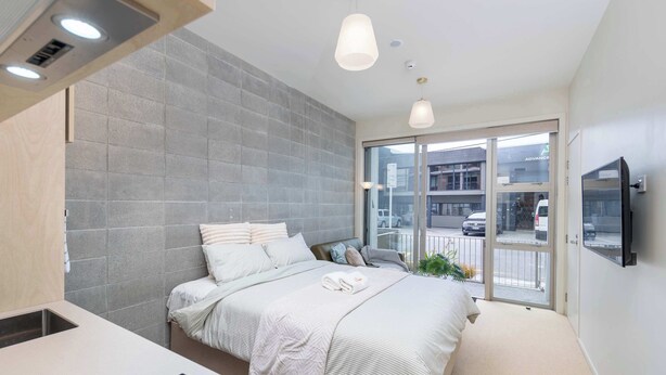 Camera da letto moderna con un letto grande, una scrivania a scomparsa e un'ampia finestra vista strada.