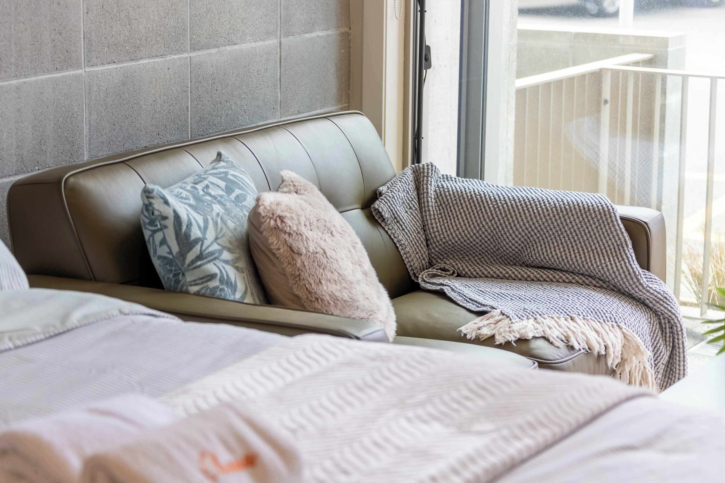 A modern living room with a leather sofa, patterned cushions, and a knitted throw blanket.