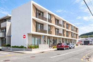 Un immeuble résidentiel à plusieurs étages, doté d’une façade plate, de balcons et d’un espace de stationnement où sont garées des voitures.