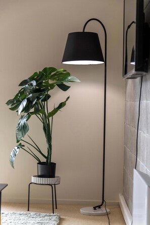 Una planta en maceta sobre un taburete pequeño al lado de una lámpara de pie en una habitación con pared de azulejos y suelo alfombrado.