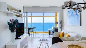 A modern living room with a large window overlooking the sea, a dining area, and a TV on a white console. - Intempo by Holuxe - 216 - 21st floor (Benidorm)