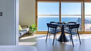 A modern living room with a large window overlooking the sea, a dining area with a table and chairs, and a sofa with a plant. - Intempo by Holuxe - 216 - 21st floor (Benidorm)