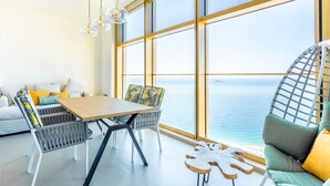 Una habitación moderna con un ventanal grande, una mesa de madera, mobiliario de mimbre y vistas al mar.