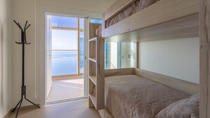 Een slaapkamer met een bed, een kapstok en een deur die leidt naar een balkon met uitzicht op zee.
