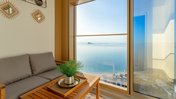 Een moderne woonkamer met een groot raam dat uitzicht biedt op de zee en een stadsgezicht.