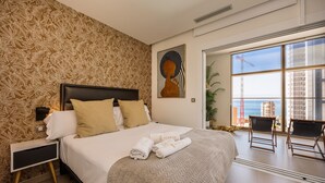 Une chambre d’hôtel avec un grand lit, une table de chevet, une fenêtre donnant sur l’océan et un tableau au mur.