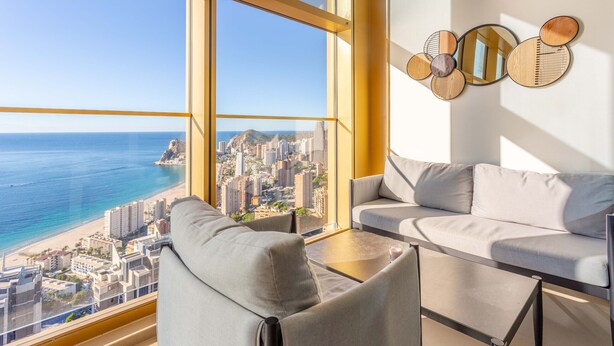 Een moderne woonkamer met een groot raam dat uitkijkt over een stadsbeeld en de zee.