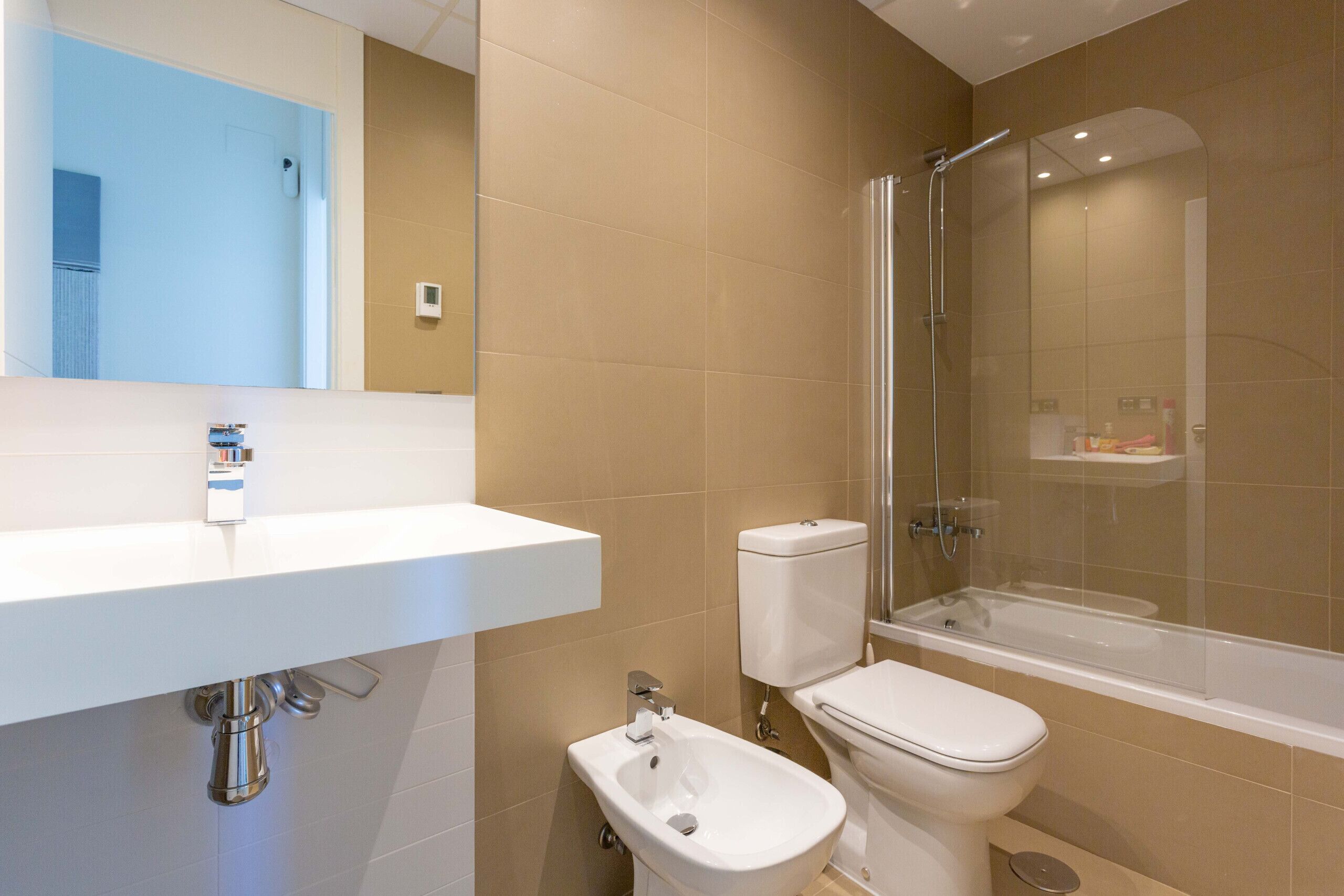 Un baño moderno con un lavamanos blanco, un bidé, un inodoro y una ducha con mampara de vidrio.