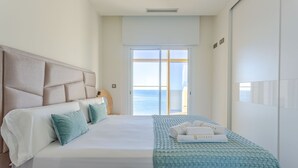 Een hotelkamer met een groot bed, uitzicht op zee door een schuifdeur en een hoofdbord met een structuur.