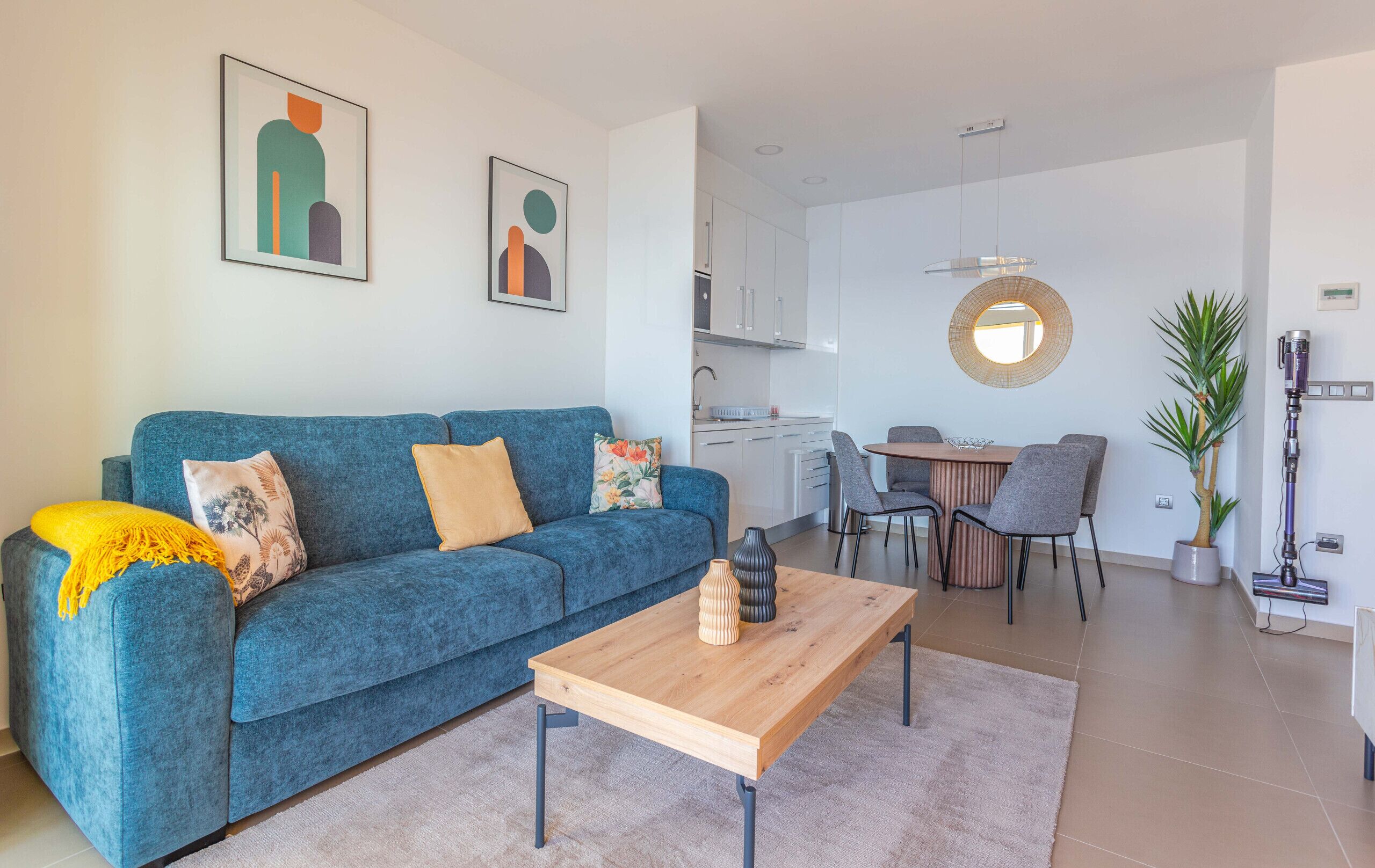 Ein modernes Wohnzimmer mit einem blauen Sofa, einem Holztisch und einer Küche im Hintergrund.