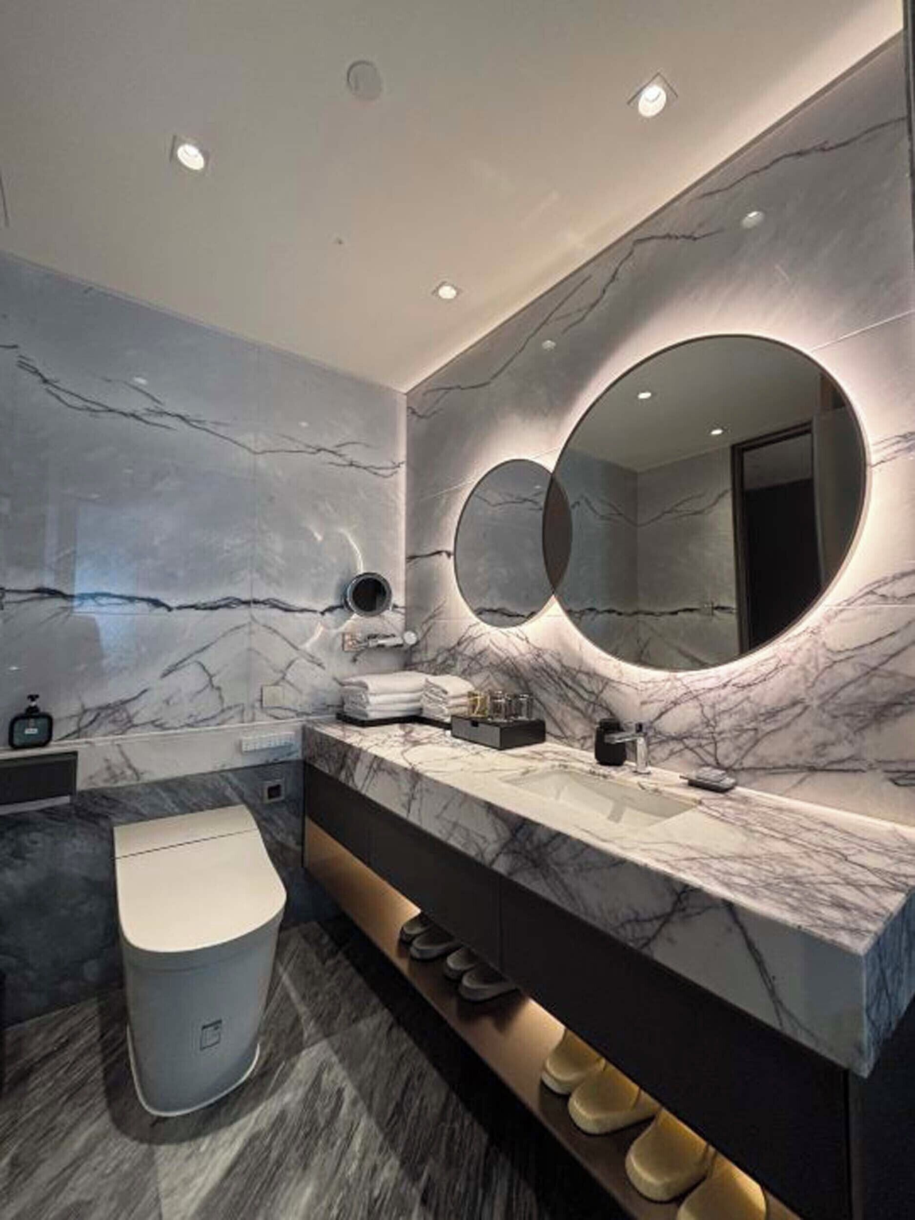 A modern bathroom with marble walls, a large mirror, and a vanity with a sink and towel rack.