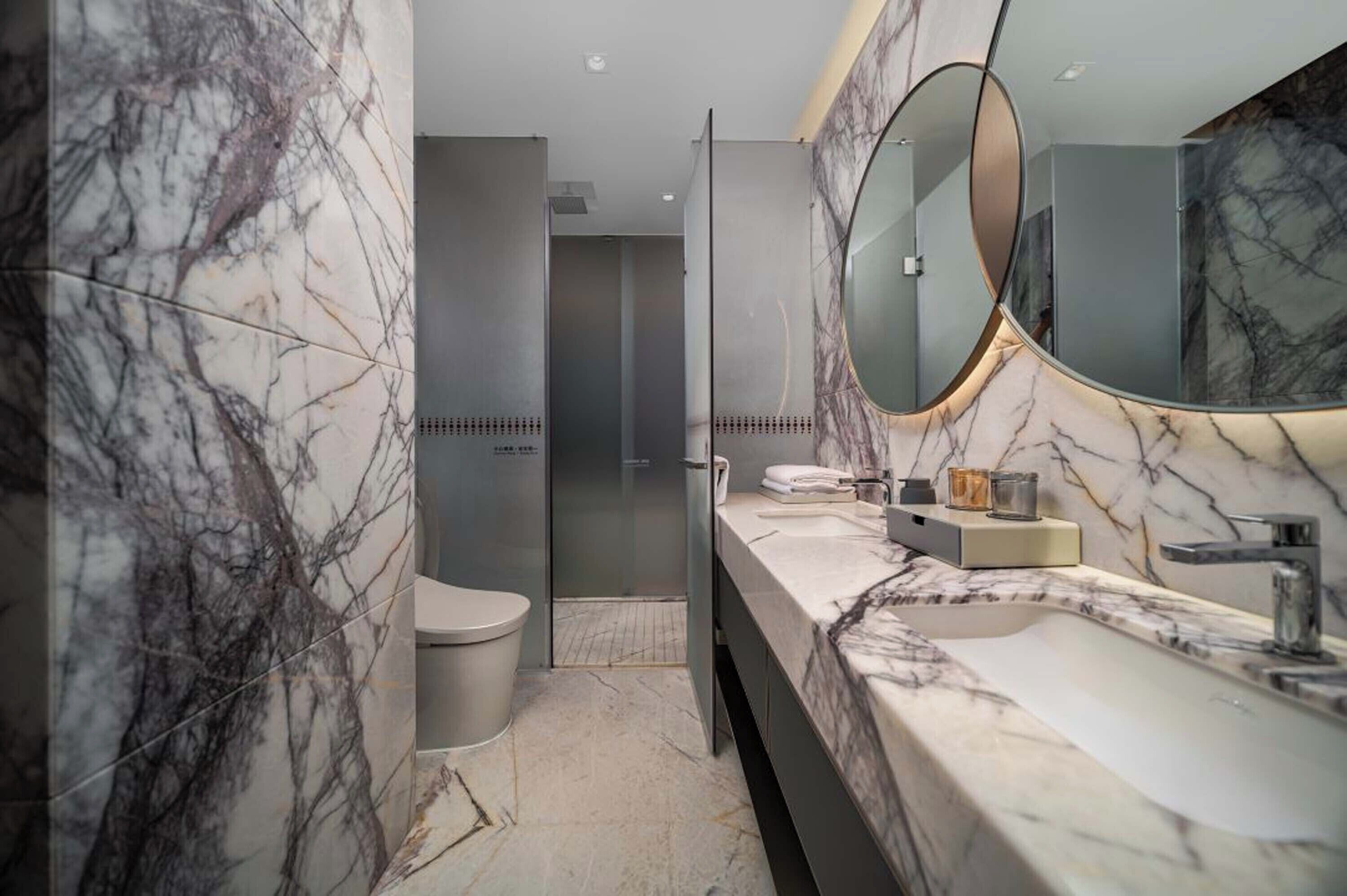 A modern bathroom with marble walls, a large mirror, and a sleek vanity.