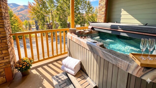 Un jacuzzi en una terraza de madera con un muro de piedra, barandilla y vistas a la montaña.