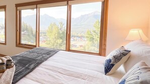 Un dormitorio con una cama grande, dos ventanas y vistas a la montaña.