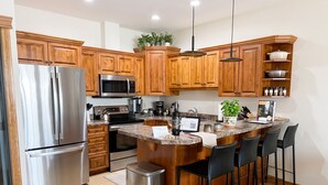 Cocina moderna con armarios de madera, electrodomésticos de acero inoxidable, encimera de granito y una zona de bar con sillas.