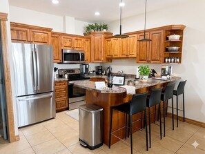 A modern kitchen with wooden cabinets, stainless steel appliances, a granite countertop, and a bar area with chairs. - Your 4-Season Adventure Base! True ski-in/ski-out 4BR condo at Sullivan Stone. Prime location on the Main Run. Features a private hot tub and a gourmet kitchen for the ultimate mountain getaway. (Kimberley)