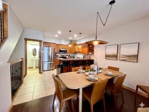 A modern kitchen with wooden cabinets, stainless steel appliances, and a dining area with a wooden table and chairs. - Your 4-Season Adventure Base! True ski-in/ski-out 4BR condo at Sullivan Stone. Prime location on the Main Run. Features a private hot tub and a gourmet kitchen for the ultimate mountain getaway. (Kimberley)