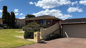 A residential driveway leading to a two-story house with a garage, surrounded by a well-maintained lawn and mature trees. - Parkview house in Hillarys. Near shops and 5 minutes to the beach (Hillarys)