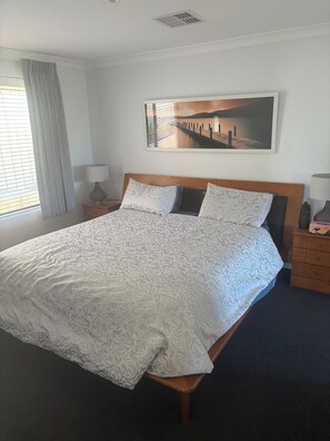 Una cama bien tendida con ropa de cama estampada, un cabecero de madera y una mesita de noche con una lámpara.