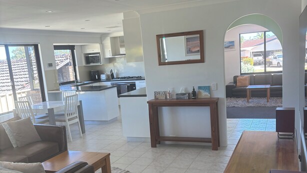 A modern living room with a sofa, coffee table, and a dining area with chairs. There is a kitchen in the background with a stove and microwave. - Parkview house in Hillarys. Near shops and 5 minutes to the beach (Hillarys)