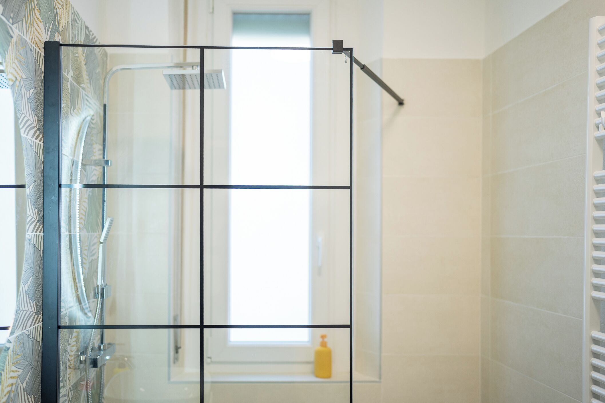 A bathroom with a glass shower enclosure, a window, and a towel rack.
