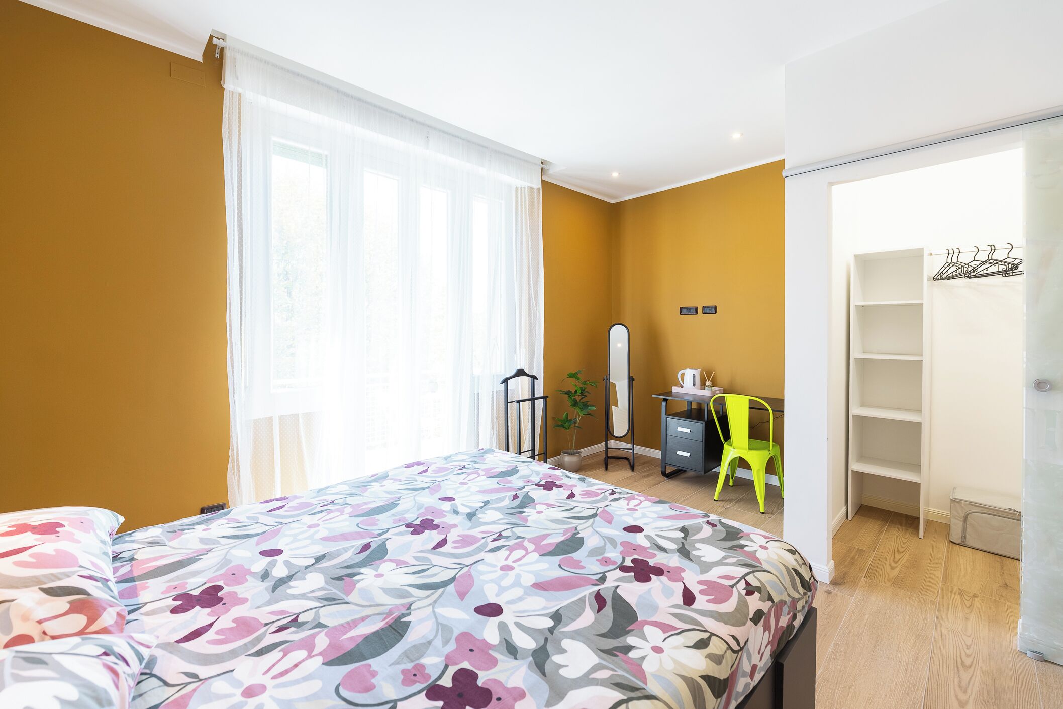 A bedroom with a floral bedspread, a bedside table with a lamp, a wardrobe, and a bright green chair.