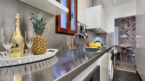 Eine moderne Küche mit Edelstahlgeräten, einer Obstschale mit Ananas und Flaschen sowie einem Essbereich mit Backsteinwand.