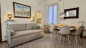 Ein Wohnzimmer mit einer Couch, einem Esstisch, Stühlen, einer Vase mit Blumen und einem Gemälde an der Wand.