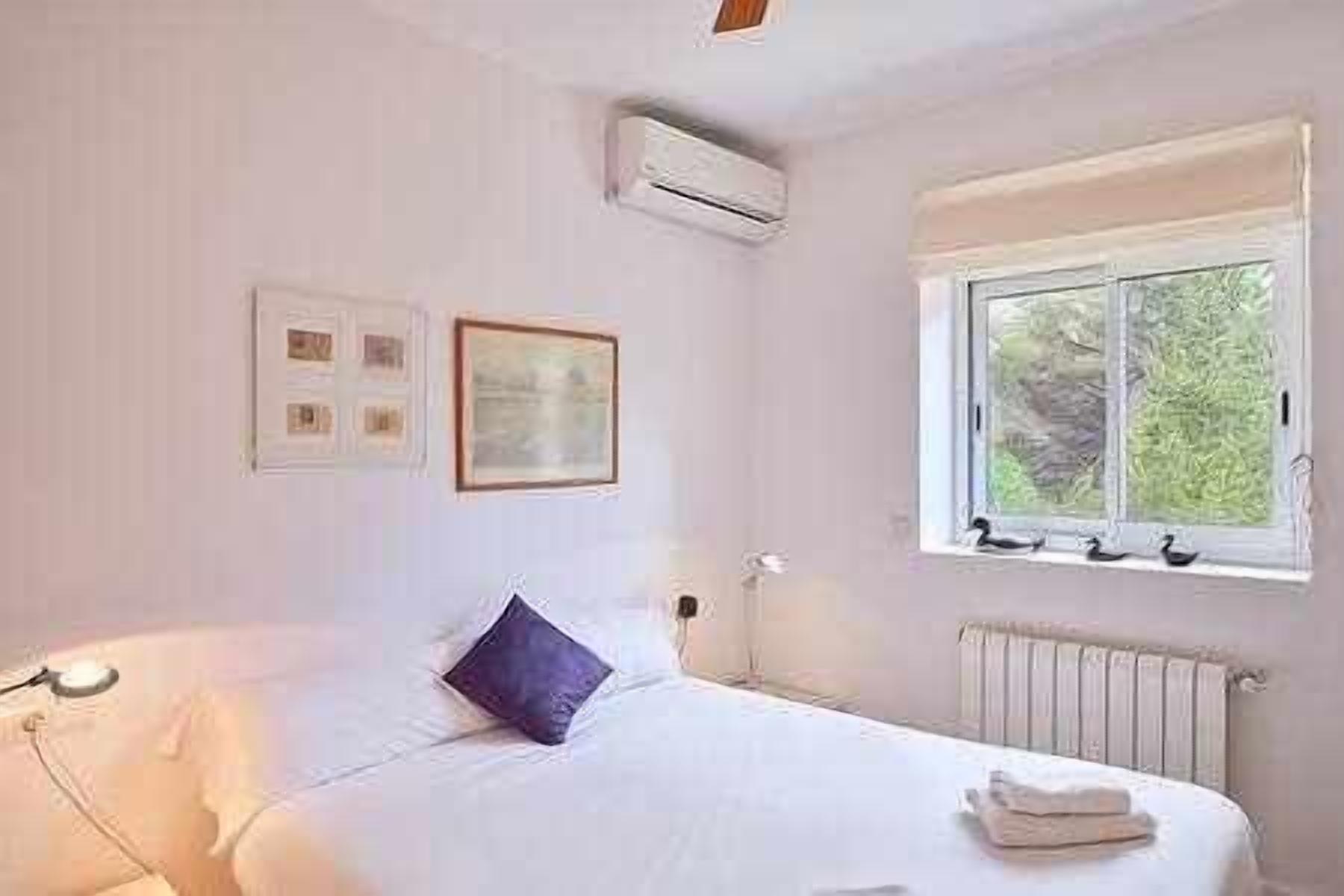 A bedroom with a bed, a window with a view of greenery, an air conditioning unit, and a radiator.