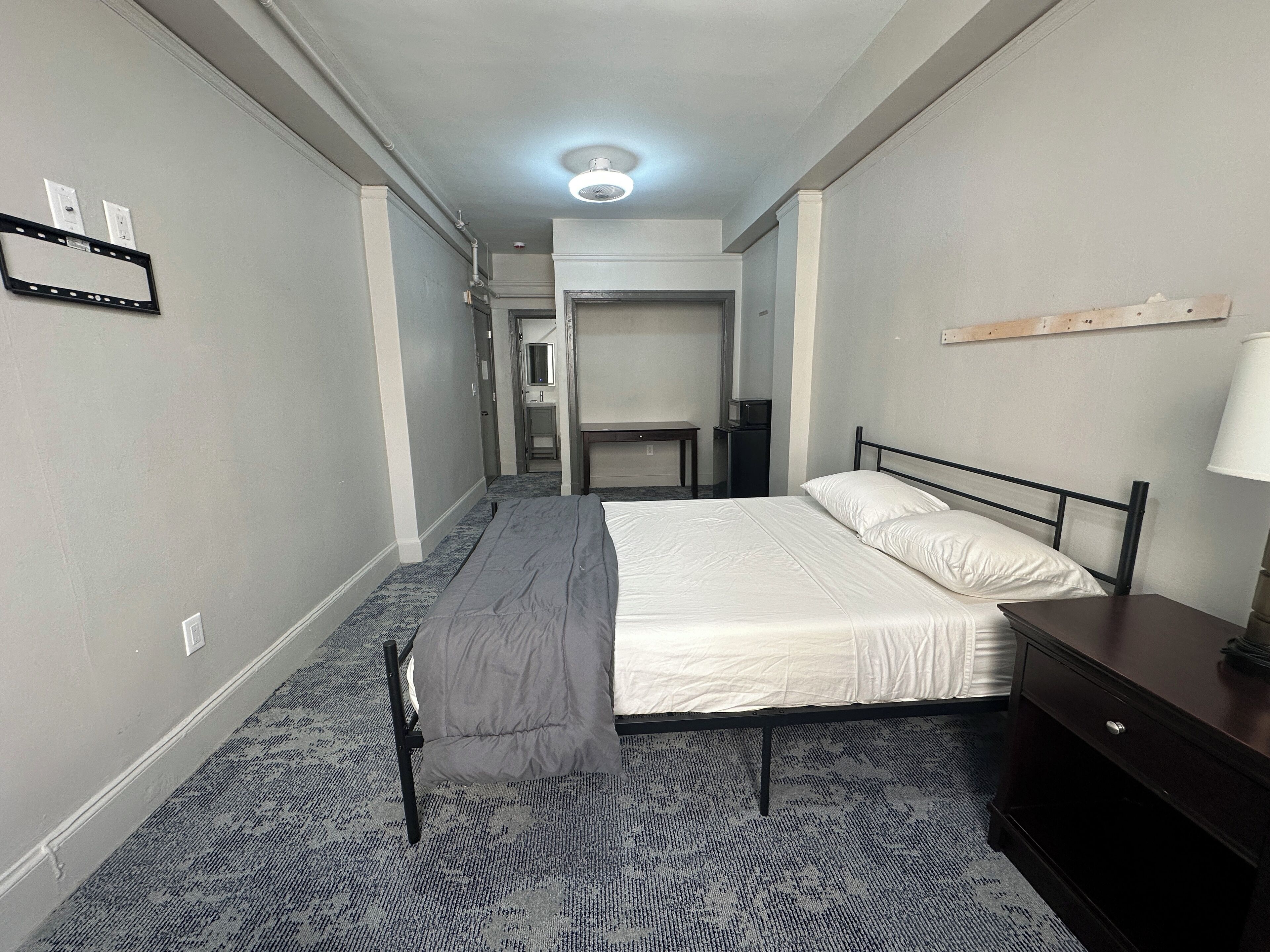 A hotel room with a bed, a desk, a chair, a lamp, and a small table.