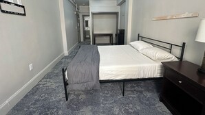Ein Hotelzimmer mit Bett, Schreibtisch, Stuhl, Lampe und einem kleinen Tisch.