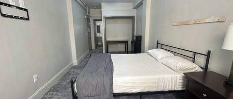 A hotel room with a bed, a desk, a chair, a lamp, and a small table.
