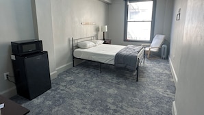 Ein Schlafzimmer mit Bett, Schreibtisch, Stuhl, Fenster und einer Mikrowelle.