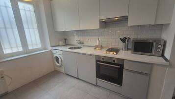 A modern kitchen with a washing machine, oven, microwave, and a window providing natural light.