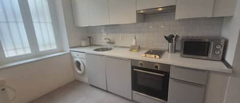 A modern kitchen with a washing machine, oven, microwave, and a window providing natural light.