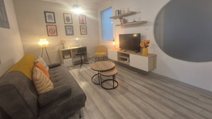 Ein modernes Wohnzimmer mit einer Couch, zwei runden Tischen, einem Fernseher und einem großen Fenster.