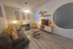 Una sala de estar moderna con un sofá, dos mesas redondas, un televisor y un ventanal grande.