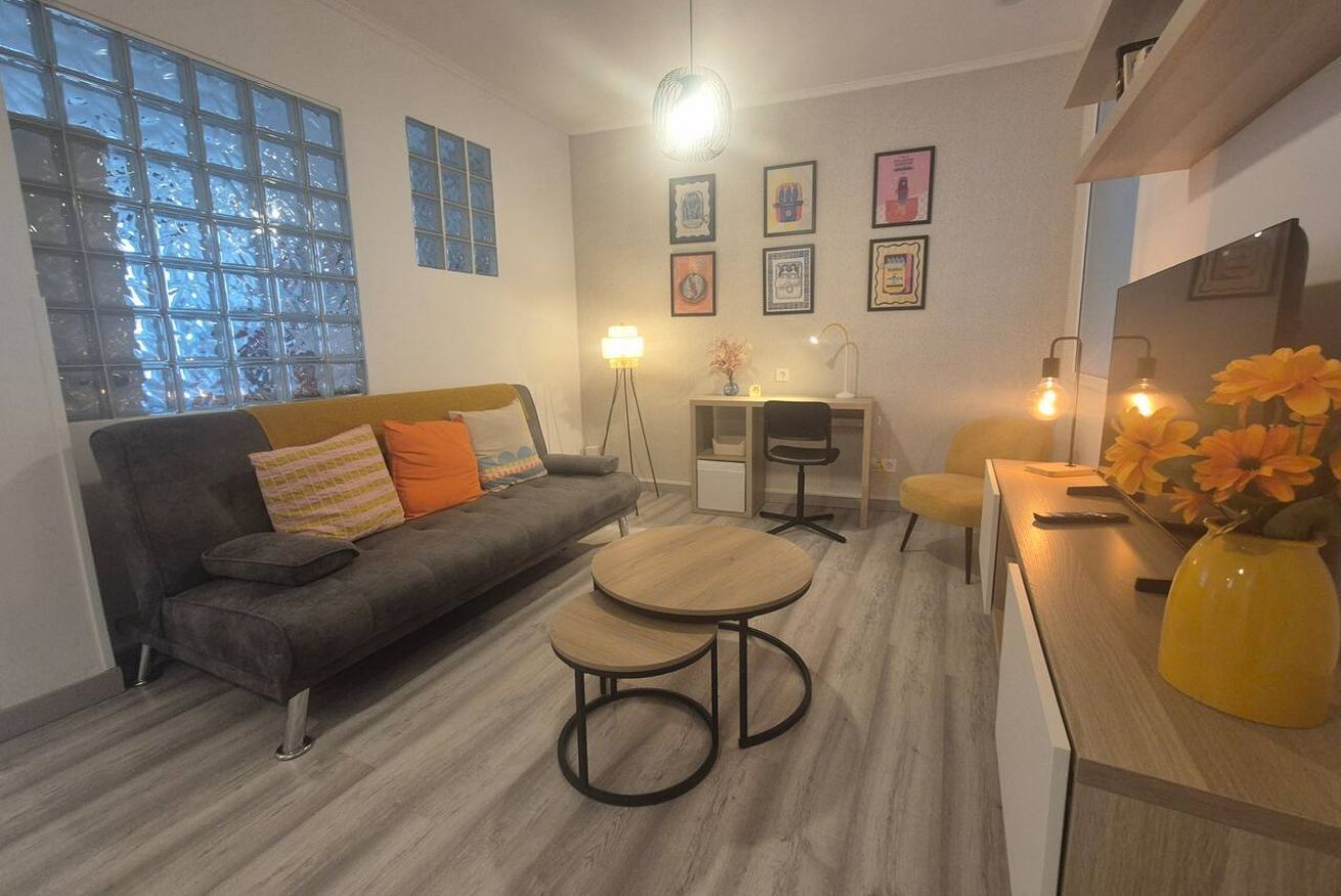 Uma sala de estar moderna com um sofá, duas mesas redondas, uma escrivaninha e uma cadeira.