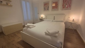 Un dormitorio con cama, mesitas de noche, lámpara de noche, espejo, ventana con cortinas y decoración en la pared.