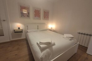Habitación de hotel con cama, mesitas de noche, cuadros en la pared y un radiador.